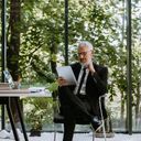 Un homme en costume est assis à une table, occupé avec une tablette.